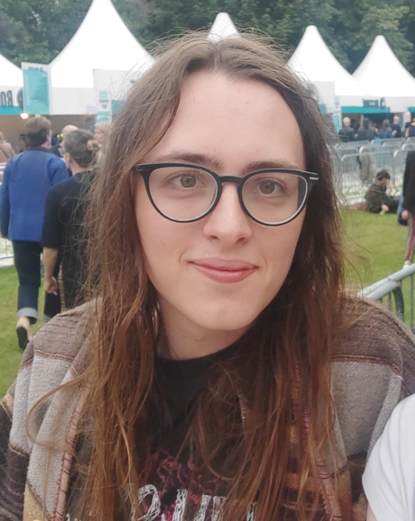 A picture of Síofra. She has long light brown hair and wears glasses with thick dark frames