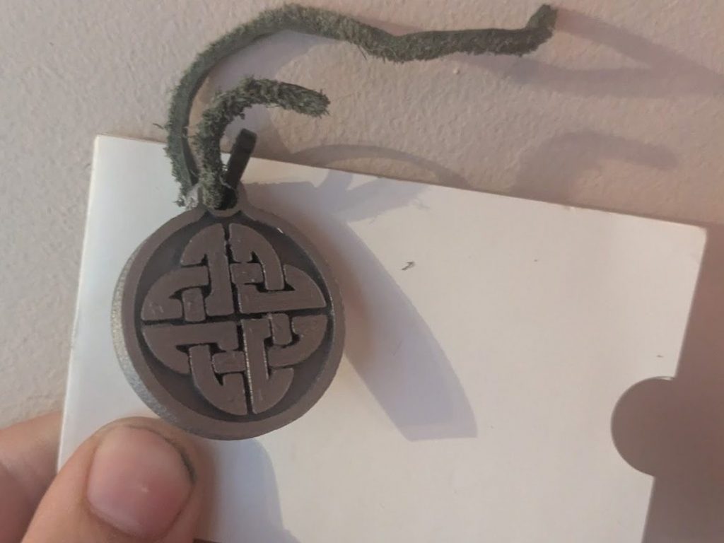 A 3D printed disk shaped token with band symbol, attached to a lammie with a piece of wool through a hole at the top