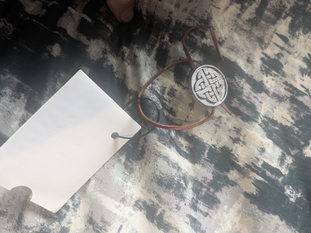 A 3D printed disk shaped token with band symbol, attached to a lammie with a piece of leather cord which passes straight through the disk from one side of the rim to the other