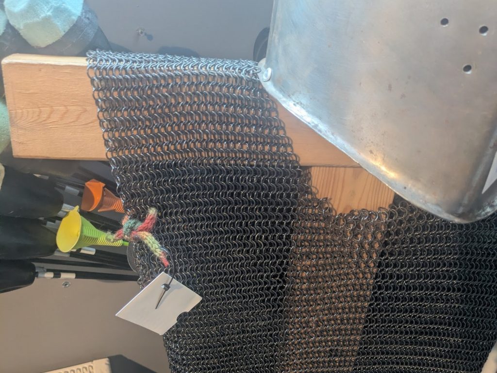 The striped woolen i-cord from the previous image is tied to chainmail armour just below the shoulder, leaving the lammie hanging in front 