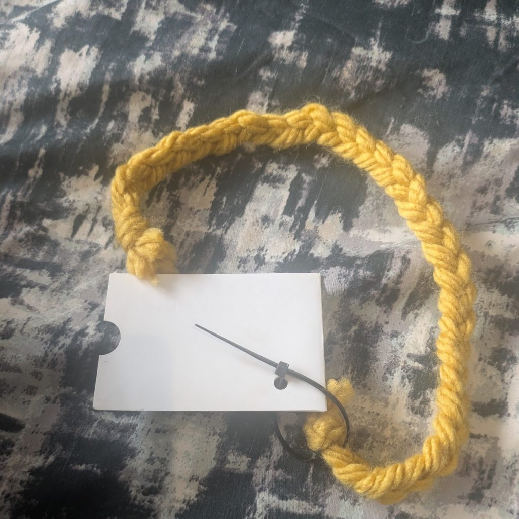 A length of braided yellow wool attached to a lammie with a cable tie just above the knot securing the braid at one end. The braid is approximately two and a half times the length of the lammie